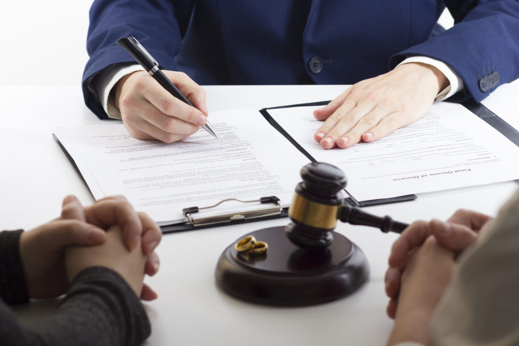 A lawyer in a suit discusses documents with clients. A gavel and wedding rings rest on the table, hinting at a legal process possibly related to divorce. This scene is common for Chicago divorce attorneys, who skillfully address complex issues like dad rights in divorce proceedings.